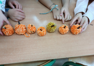 8 pomarańczowych dyni z włóczki leżących na ławce.