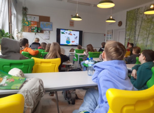 Uczniowie siedzą na kolorowych krzesłach i oglądają prezentację o tematyce ekologicznej.