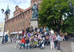 Uczniowie pozują pod pomnikiem Mikołaja Kopernika.