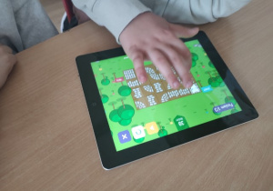 Tablet leżący na drewnianym blacie stołu.