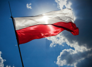 Flaga Polski zatknięta na maszcie na tle błękitnego nieba.