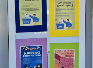 Nowa tablica ogłoszeniowa na szklanych drzwiach naszej szkoły, pełna kolorowych plakatów i ogłoszeń.