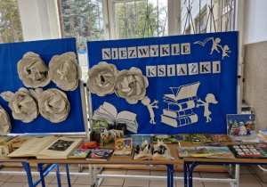 Szkolne ławki z wyłożonymi na nich książkami i dekoracja wydarzenia z napisem Niezwykłe ksiażki.