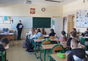 Uczniowie klasy 5a słuchają tekstu wiersza czytanego przez kolegę z ich klasy.