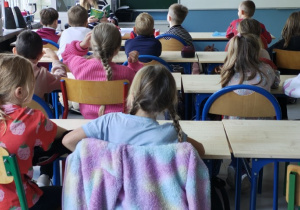 Uczniowie klasy 2a uważnie słuchają czytanego przez koleżankę ze starszej klasy fragmentu książki pt. „Karolcia” M. Kruger.