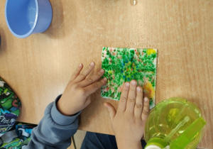 Uczeń rozciera kolory na swojej pracy po zmoczeniu papieru.
