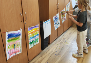 Uczennice malują farbami na rozwieszonym papierze.