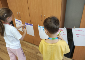 Uczniowie malują farbami na rozwieszonym na sznurku papierze.