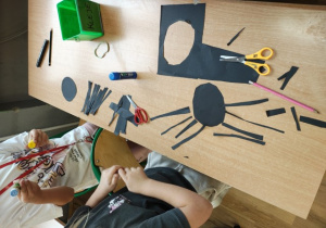 Uczniowie wycinają pająki z czarnego papieru.