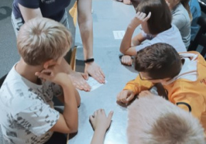 Uczniowie klasy 4b siedzą przy stołach i patrzą w stronę osoby prowadzącej zajęcia.