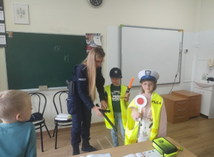 Dwaj uczniowie klasy 1b w strojach policyjnych wraz z prowadzącą zajęcia policjantką.