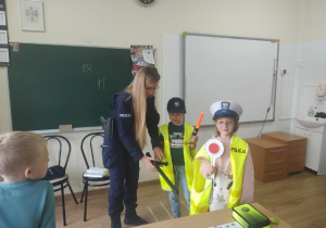 Dwaj uczniowie klasy 1b w strojach policyjnych wraz z prowadzącą zajęcia policjantką.