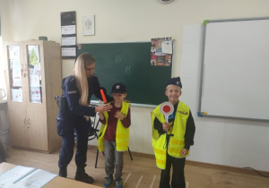 Dwaj uczniowie klasy 1b w strojach policyjnych wraz z prowadzącą zajęcia policjantką.