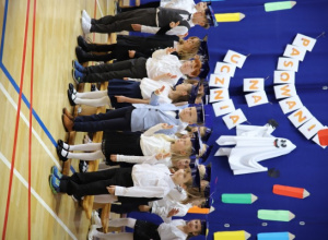 Pierwszoklasiści w galowych strojach stoją na tle dekoracji z okazji pasowania na ucznia.