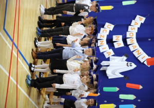 Pierwszoklasiści w galowych strojach stoją na tle dekoracji z okazji pasowania na ucznia.