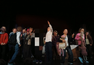 Uczniowie odgrywają scenkę na scenie wraz z aktorami.