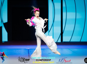 Nikola tańczy na scenie w białym stroju.