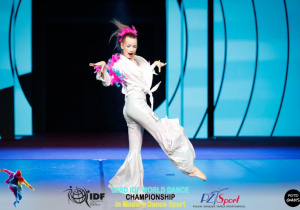 Nikola tańczy na scenie w białym stroju.