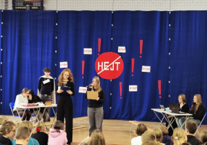 Uczniowie z klasy 8A na scenie podczas inscenizacji ilustrujących zjawisko hejtu w różnych kontekstach.