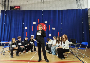 Uczniowie siedzą na ławce podczas debaty, w której uczestnicy na scenie podsumowali całe wydarzenie i przypomnieli o zasadach reagowania na hejt.