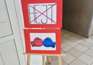 Plakaty przygotowanę przez Wiktorię Hraneczny z klasy 8A, przywieszone na sztaludze.