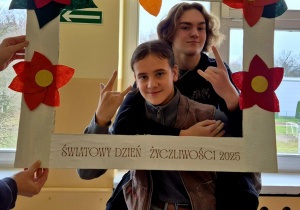 Dwóch chłopców pozujących do zdjęcia w ramce z napisem “Światowy Dzień Życzliwości 2025”