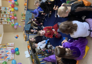 Dzieci siedzą w kole na dywanie, po środku siedzi chłopiec, który im wróży