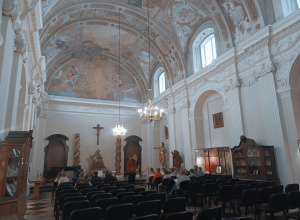 Uczniowie siedzą w ławkach w katedrze łowickiej która ma ręcznie malowany sufit i ozdobne sklepienia.