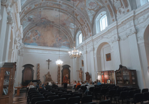 Uczniowie siedzą w katedrze łowickiej która ma ręcznie malowany sufit i ozdobne sklepienia.