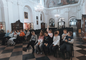 Uczniowie siedzą w katedrze łowickiej i słuchają prezentacji.