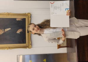 Uczennica z dyplomem Stypendium Prezydenta Miasta Łodzi „Mia 100 Zdolnych”, na tle portretu patrona naszej szkoły – Aleksego Rżewskiego.