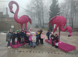 Uczniowie klasy 1 b pozują na tle 2 olbrzymich, różowych flamingów.