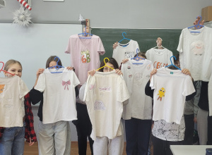 Grupa uczniów z klasy 6 a prezentuje koszulki z nadrukami.