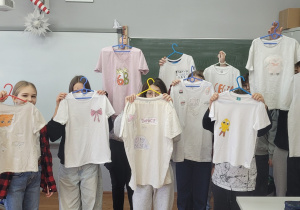 Grupa uczniów z klasy 6 a prezentuje koszulki z nadrukami.