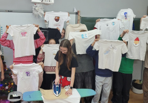 Grupa uczniów z klasy 6 b prezentuje koszulki z nadrukami.