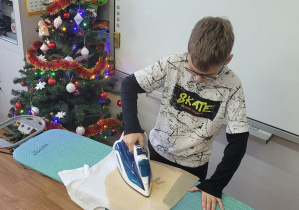 Uczeń klasy szóstej wykonuje nadruk na koszulce prasując żelazkiem.