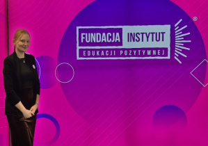 Pani Kinga Blachowska pozująca do zdjęcia na ściance z napisem “Fundacja Instytut Edukacji Pozytywnej”.
