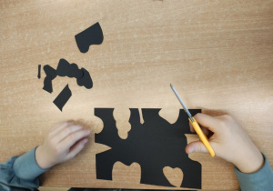 Uczeń wycina kształty z czarnego papieru.