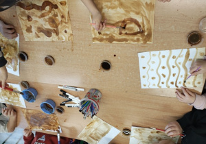 Uczniowie malują tło kawą.