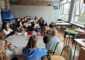 Uczniowie siedzą wokół dwóch stołów i słuchają koleżanki opowiadającej o tym jak zaczęła się jej przygoda z szydełkiem.