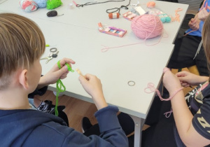 Uczniowie dziergają łańcuszek z kolorowych włóczek.