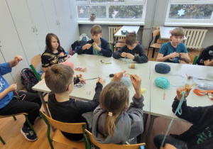 Uczniowie dziergają łańcuszek z kolorowych włóczek.