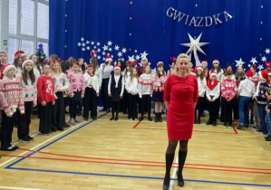 Dyrygentka chóru, zachęca publiczność do wspólnego zaśpiewania kolędy