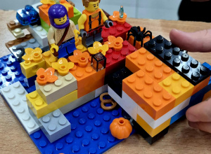 Kolorowa budowla z ludzikami LEGO, plastikowymi dyniami i pająkiem.