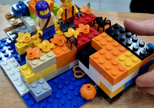 Kolorowa budowla z ludzikami LEGO, plastikowymi dyniami i pająkiem.