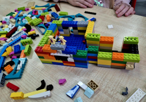 Wielokolorowy domek z LEGO, którego na murach strzegą dwa małe plastikowe misie.