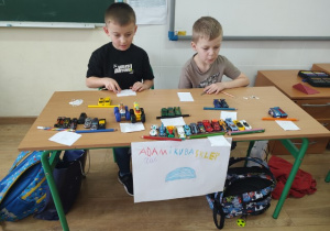 Uczniowie klasy 1b szykują wystawę sklepiku z samochodami.
