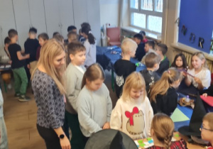 Dzieci oraz nauczycielka stoją przy stacjach z wróżbami .