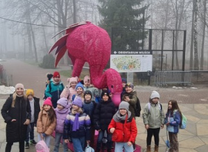 Uczniowie wraz z nauczycielem stoją przy ogromnym różowym flamingu.