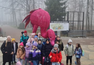 Uczniowie wraz z nauczycielem stoją przy ogromnym różowym flamingu.